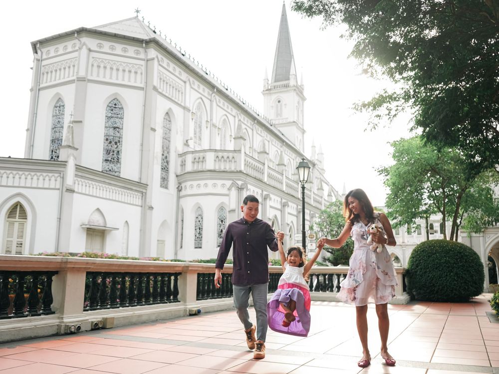 People walk and play on a church courtyard with white cathedral architecture visible in the background.