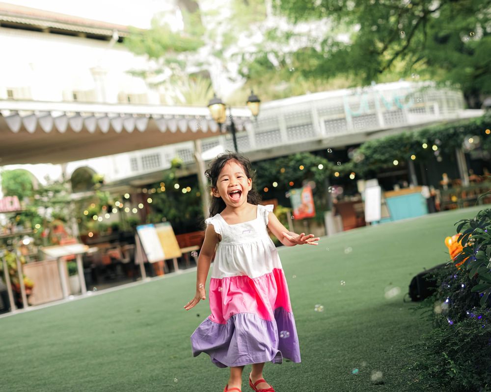 A series of outdoor playground photos showing children playing and running on green turf under string lights.