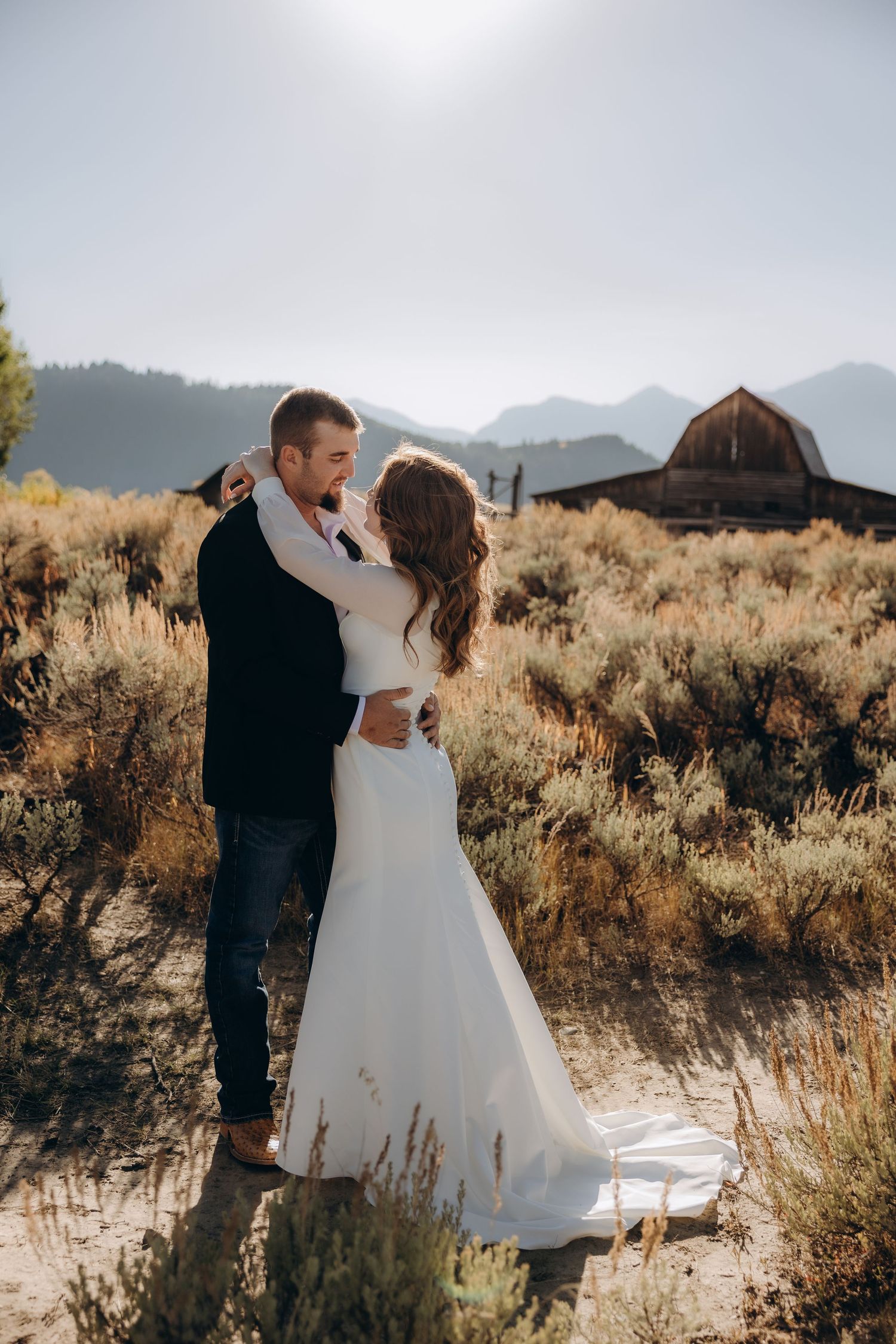 A couple embraces in a desert landscape with golden sagebrush and mountains in the background at sunset.