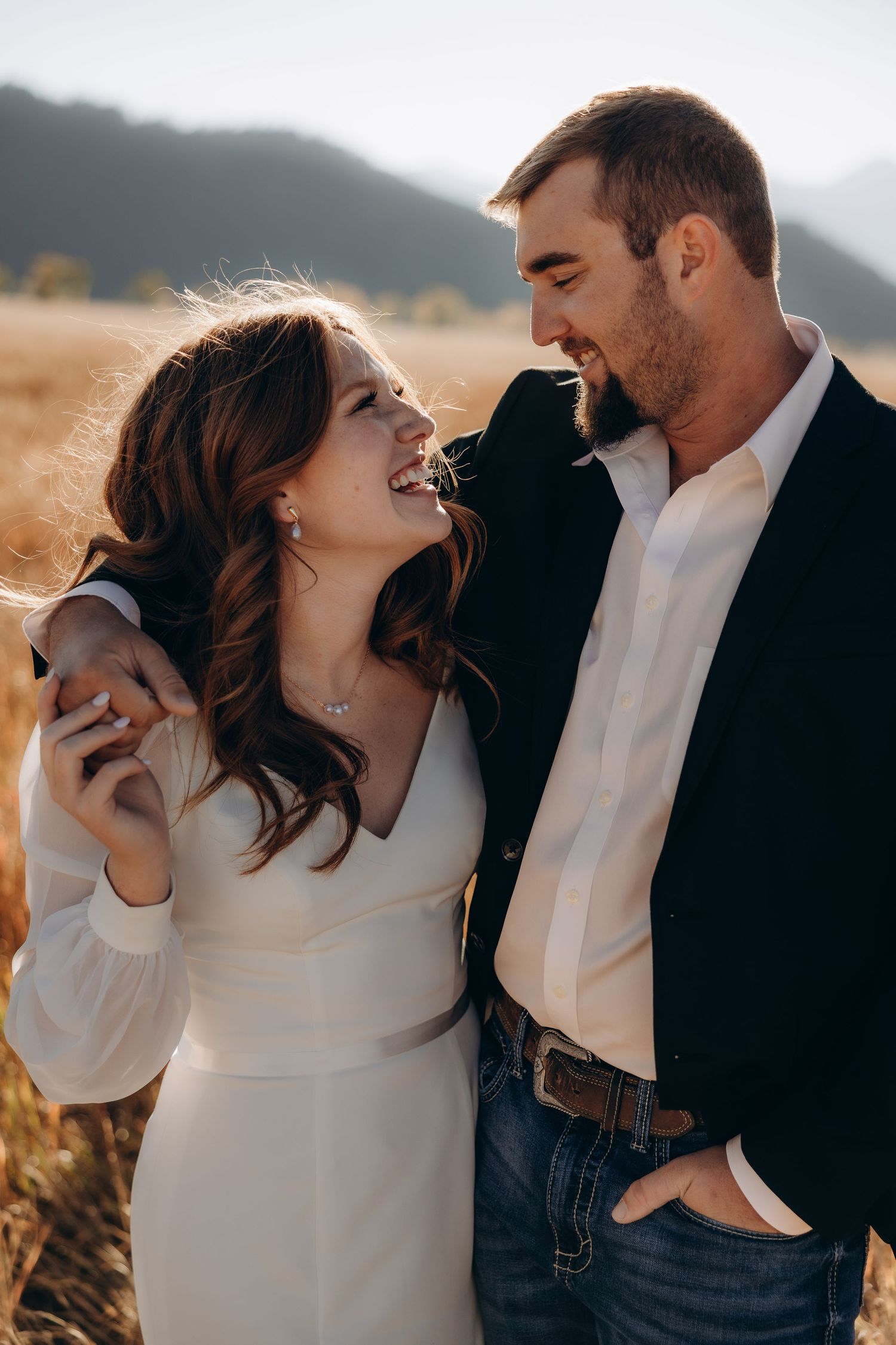 Romantic couple in white and black outfits sharing intimate moments in a golden field during sunset.