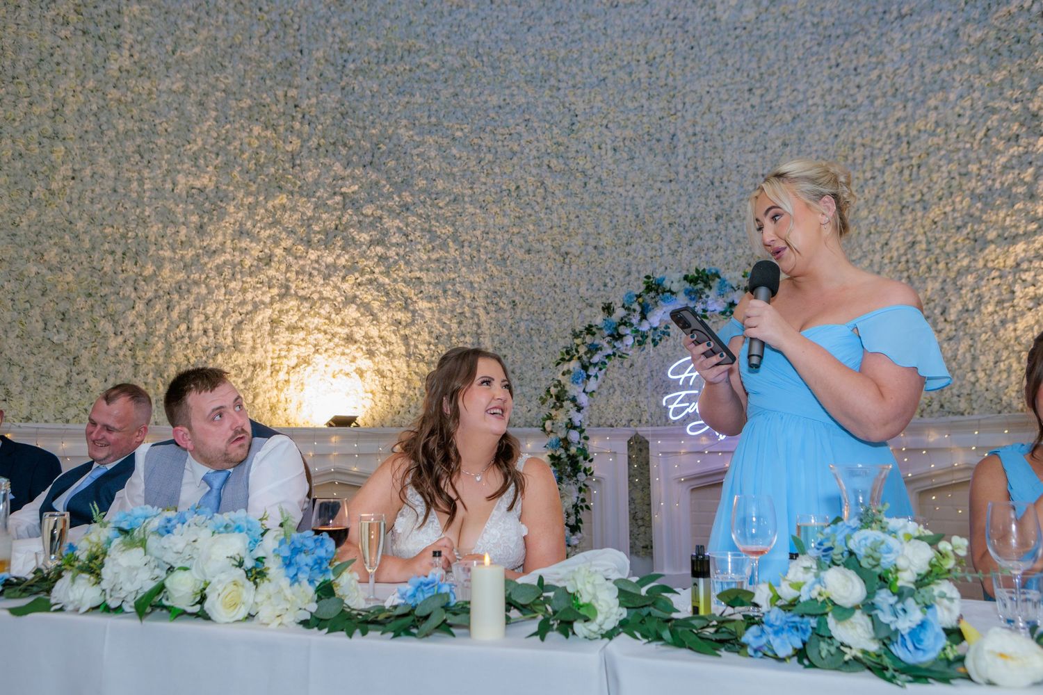 Wedding party guests seated at a long table decorated with blue and white floral centerpieces during a reception.
