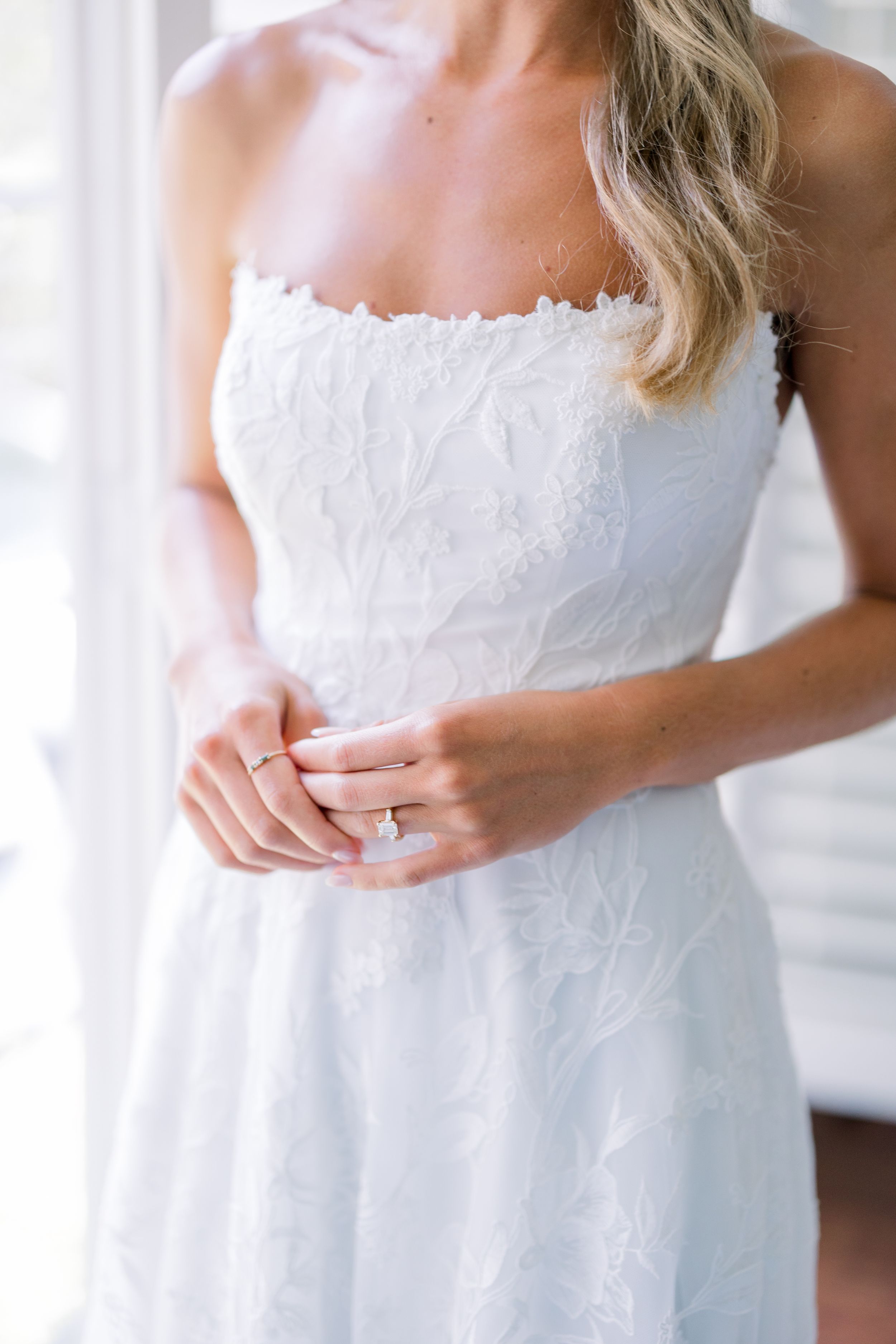 Close up detail of delicate white lace wedding dress bodice and engagement ring.