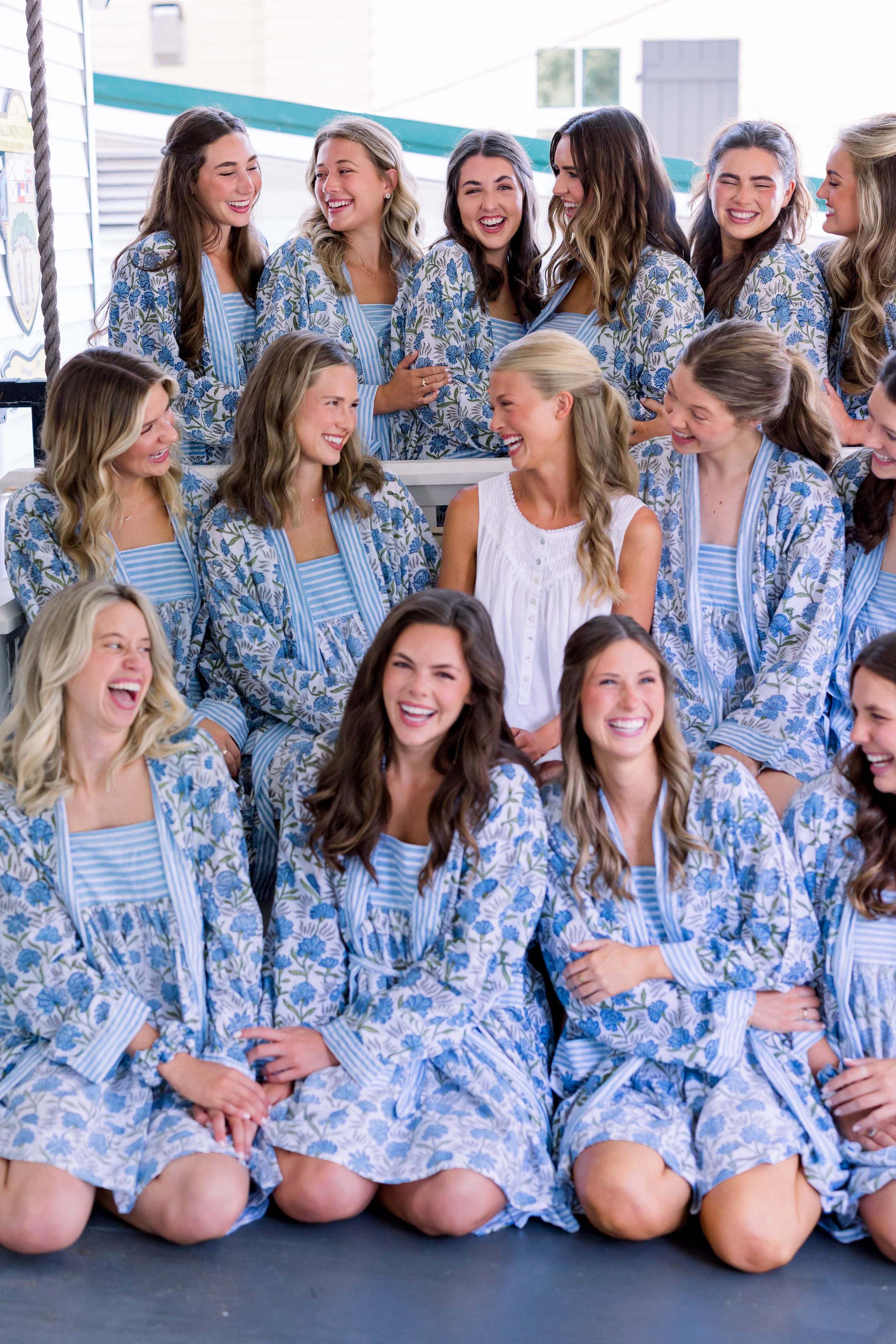 Large group wearing matching blue and white floral robes pose together for wedding party photo.