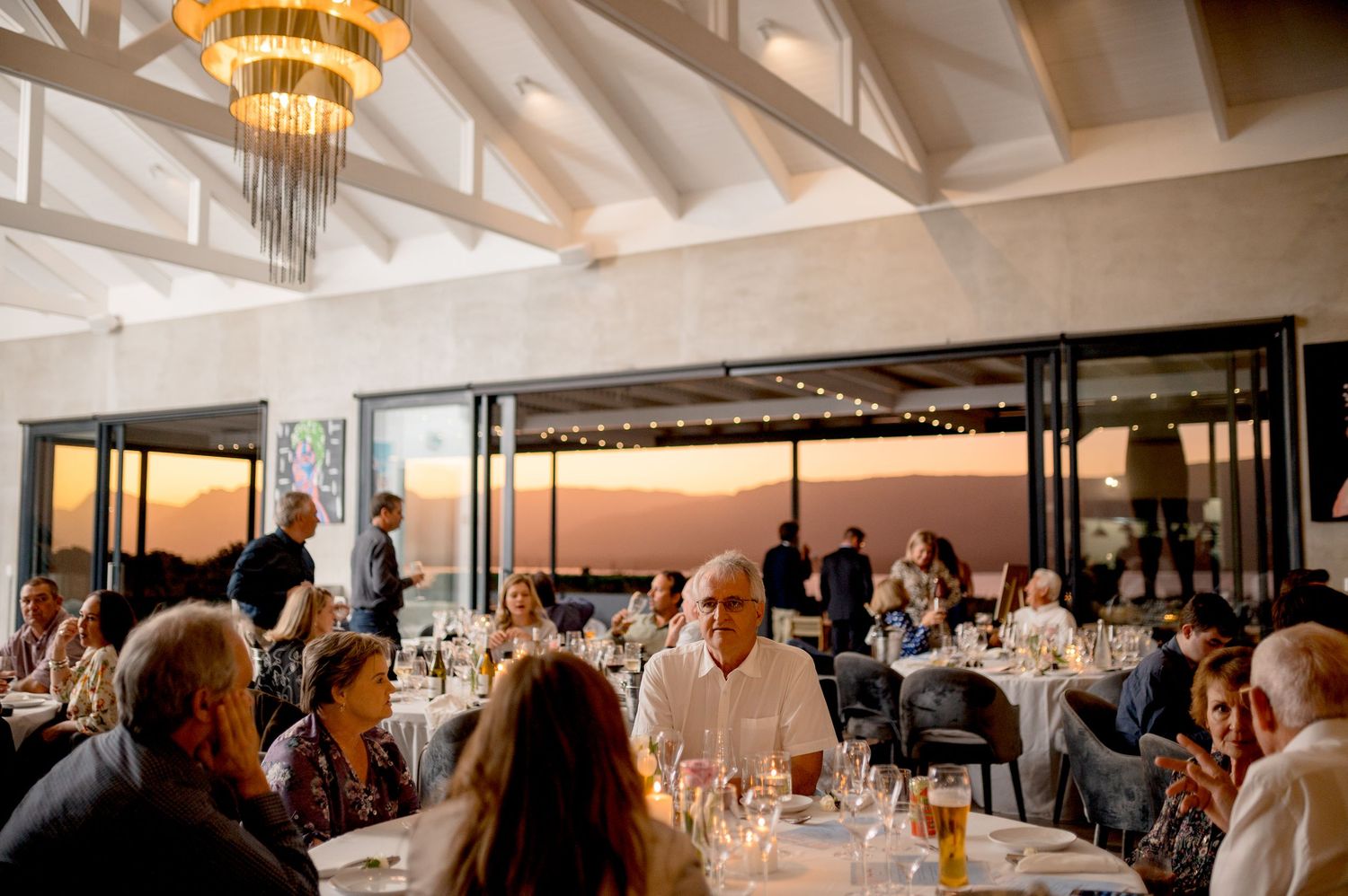 A panoramic view of an elegant wedding reception venue with white decor, exposed beams, and dining tables.