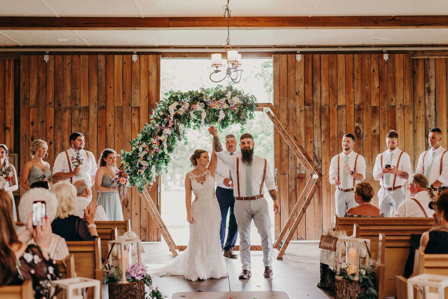 Wedding party poses in sequence inside a rustic wooden barn venue with decorative floral accents.