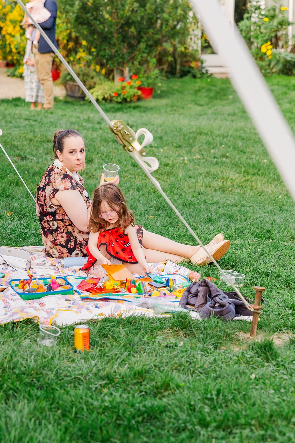 People enjoying a summer picnic on a blanket in a lush backyard garden with colorful food and drinks spread out.