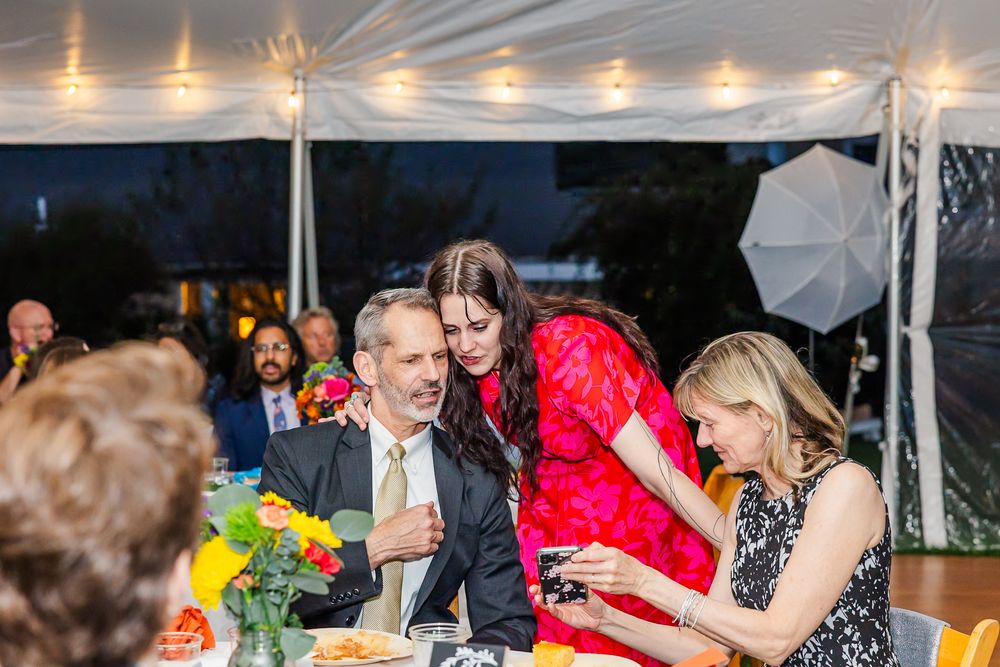 Wedding guests dance and celebrate under a white tent during an evening reception with glowing lights.