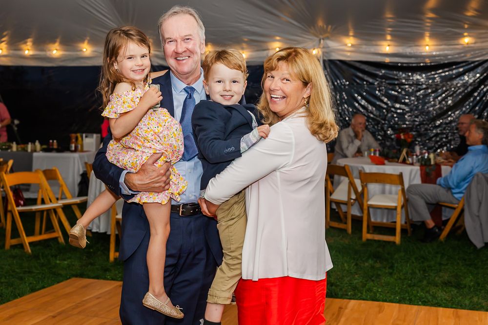 A group celebrates joyfully at an outdoor wedding reception under string lights and a tent.