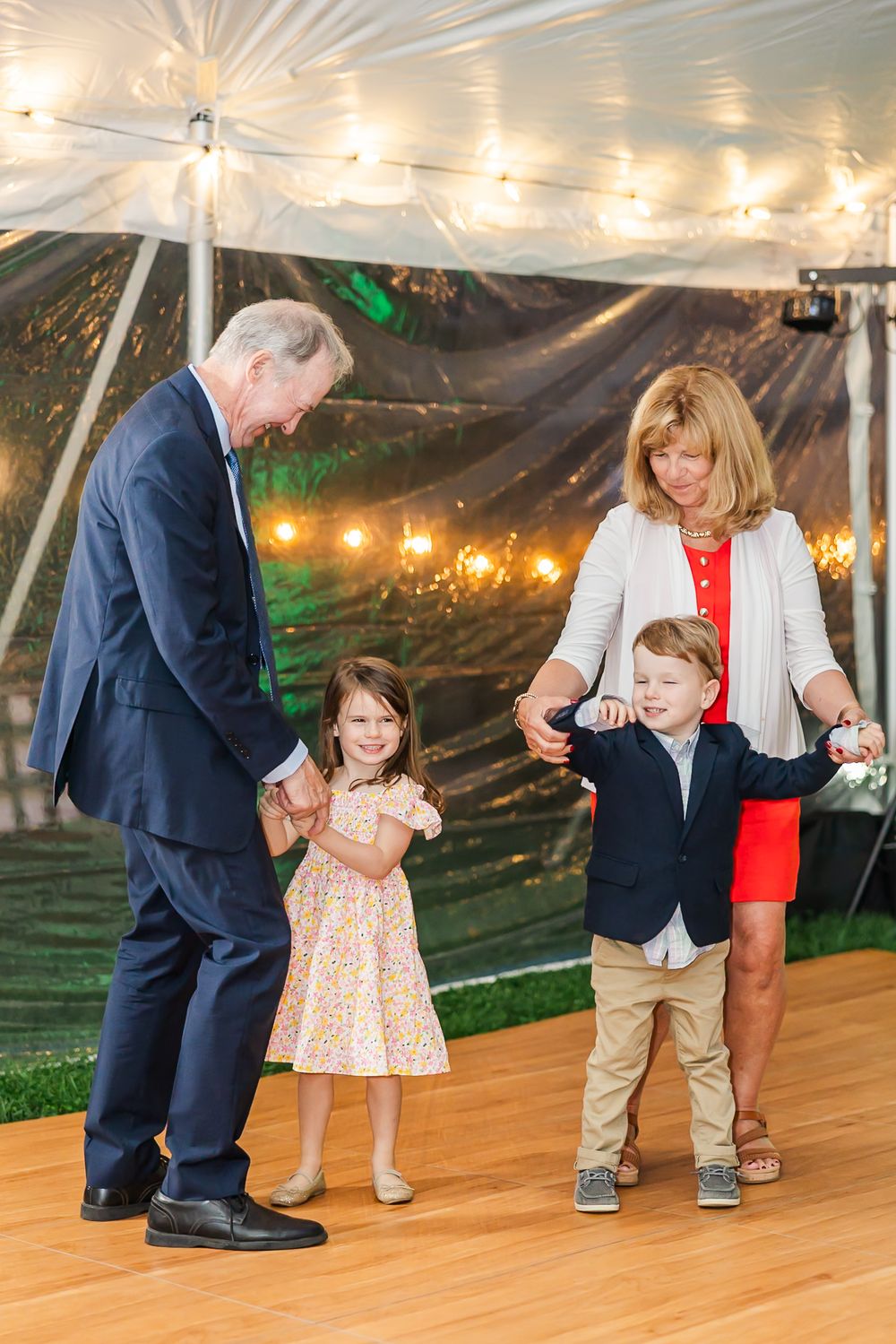 People dancing and celebrating at a wedding reception under a white tent with string lights overhead.