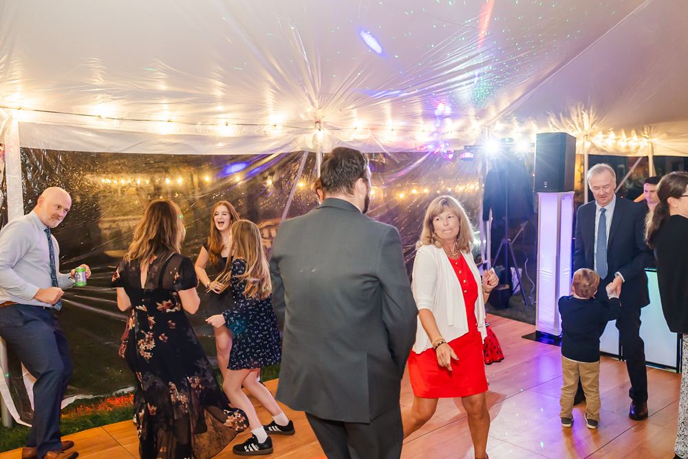Wedding guests dance and celebrate on a festively lit dance floor under string lights at an evening reception.
