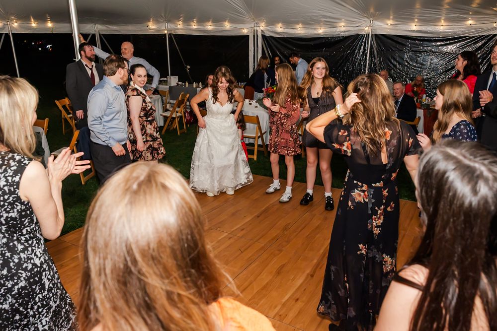 A group of people dancing and celebrating on a wooden dance floor under string lights at a festive event.