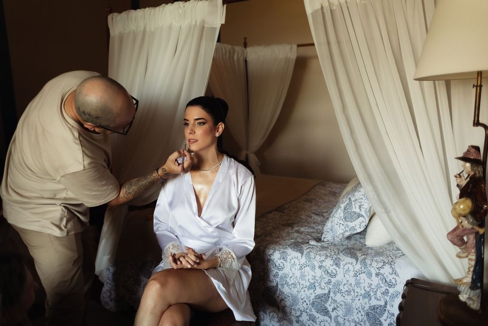 A romantic couple in white attire shares tender moments on a bed with white linens and curtains.