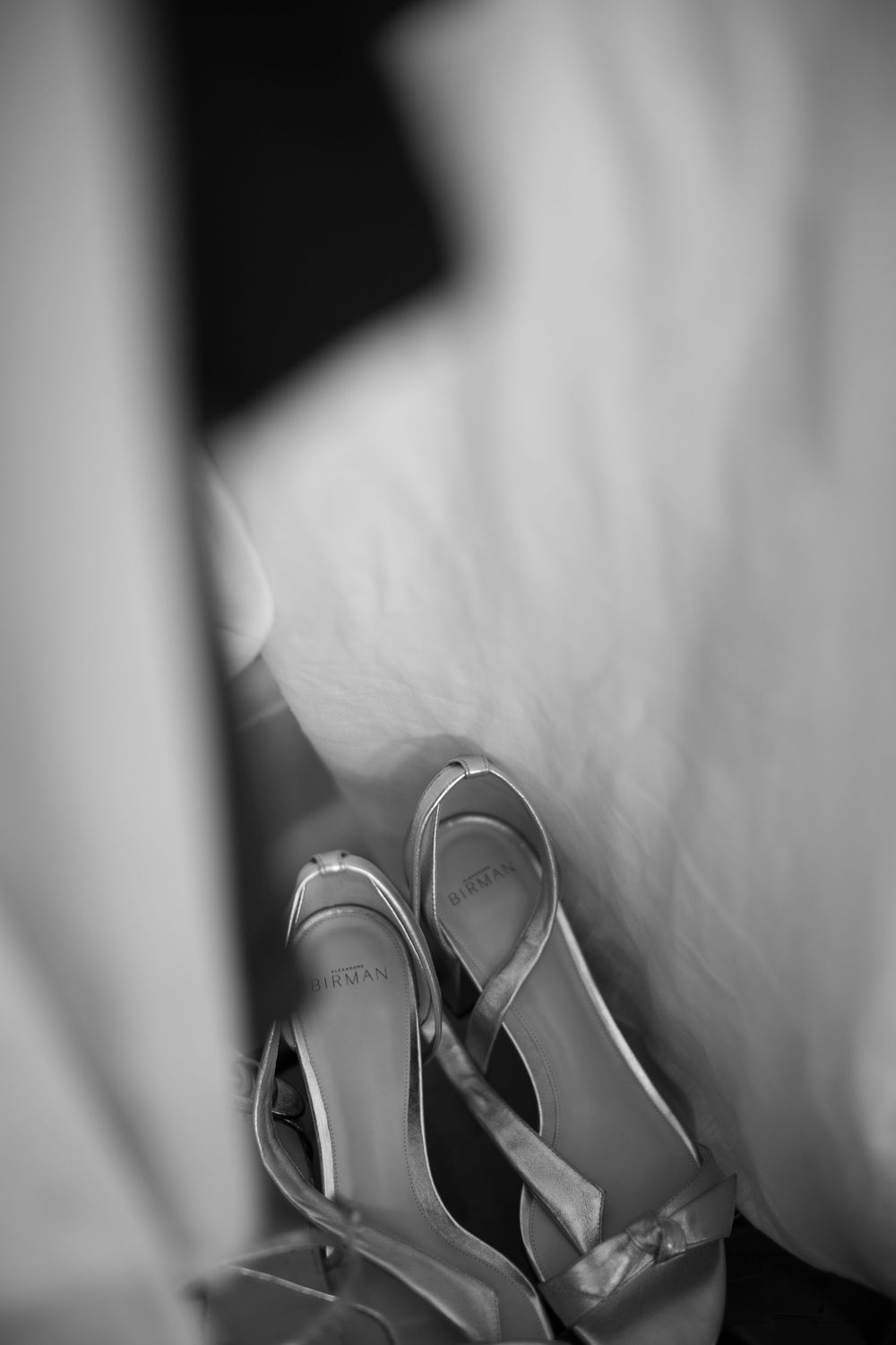 Elegant bridal heels in soft focus black and white photography against white fabric.