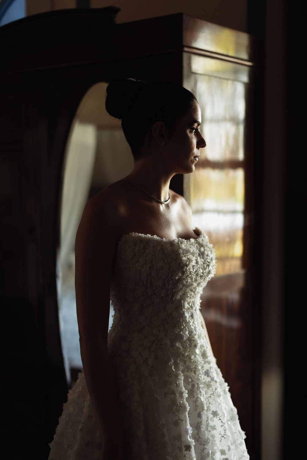 A stunning white lace wedding dress with intricate beading detail is photographed in dramatic lighting.