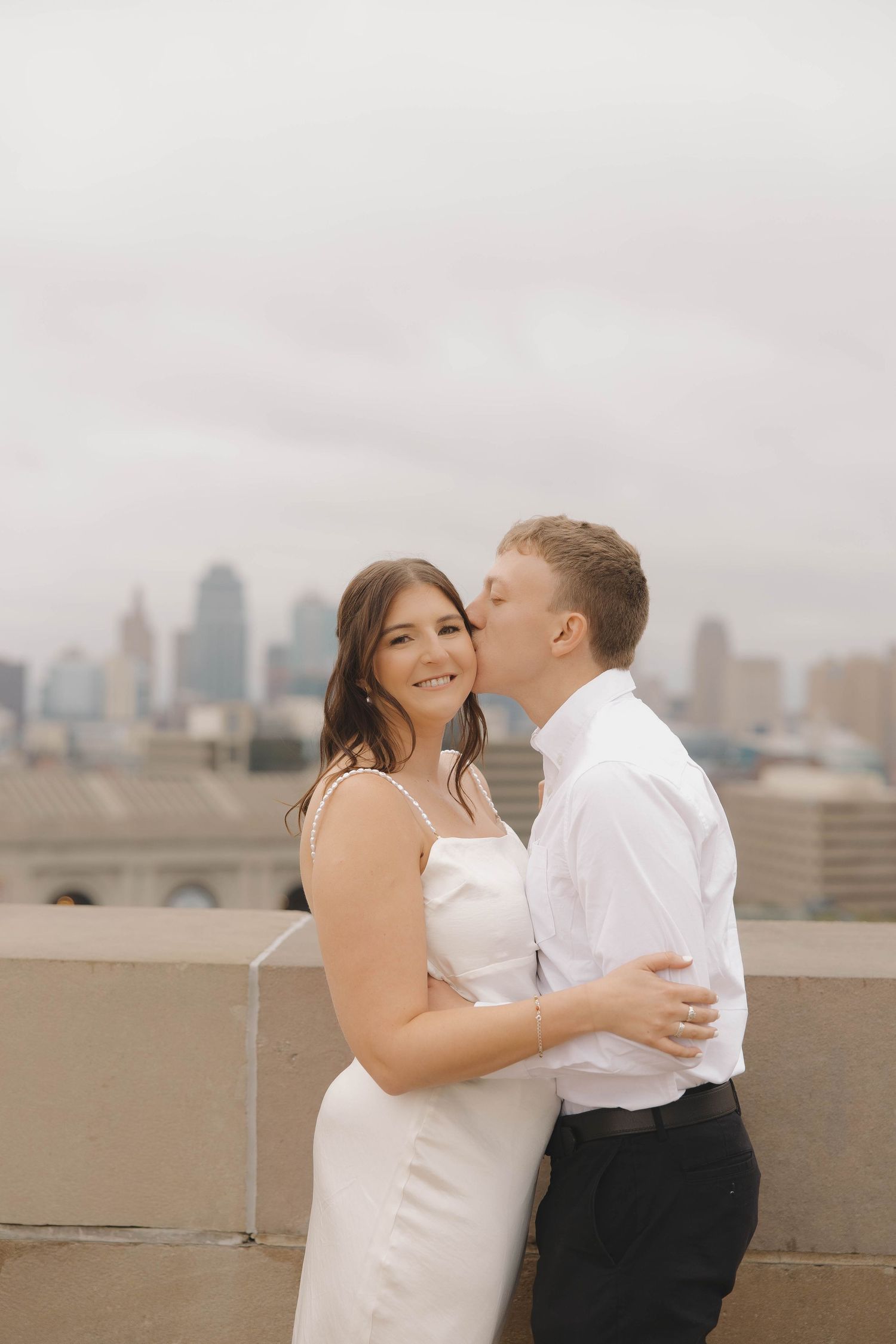 A romantic rooftop moment with a city skyline backdrop as a couple embraces in wedding attire.