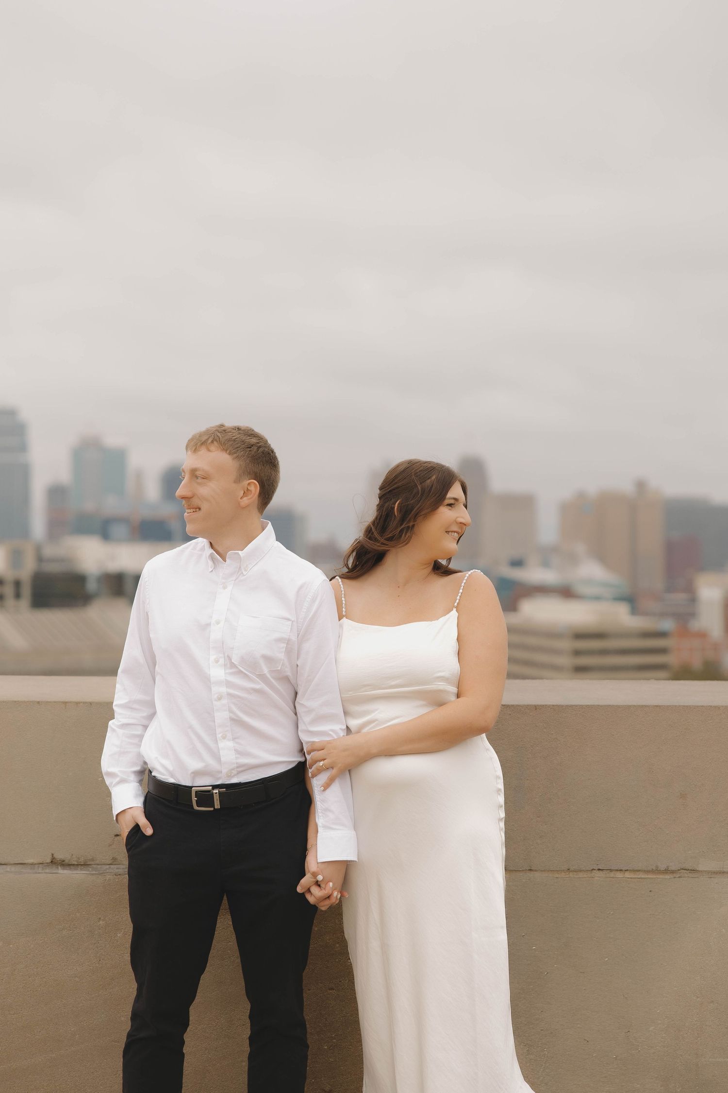 A couple in wedding attire share intimate moments on a city rooftop with an urban skyline in the background.