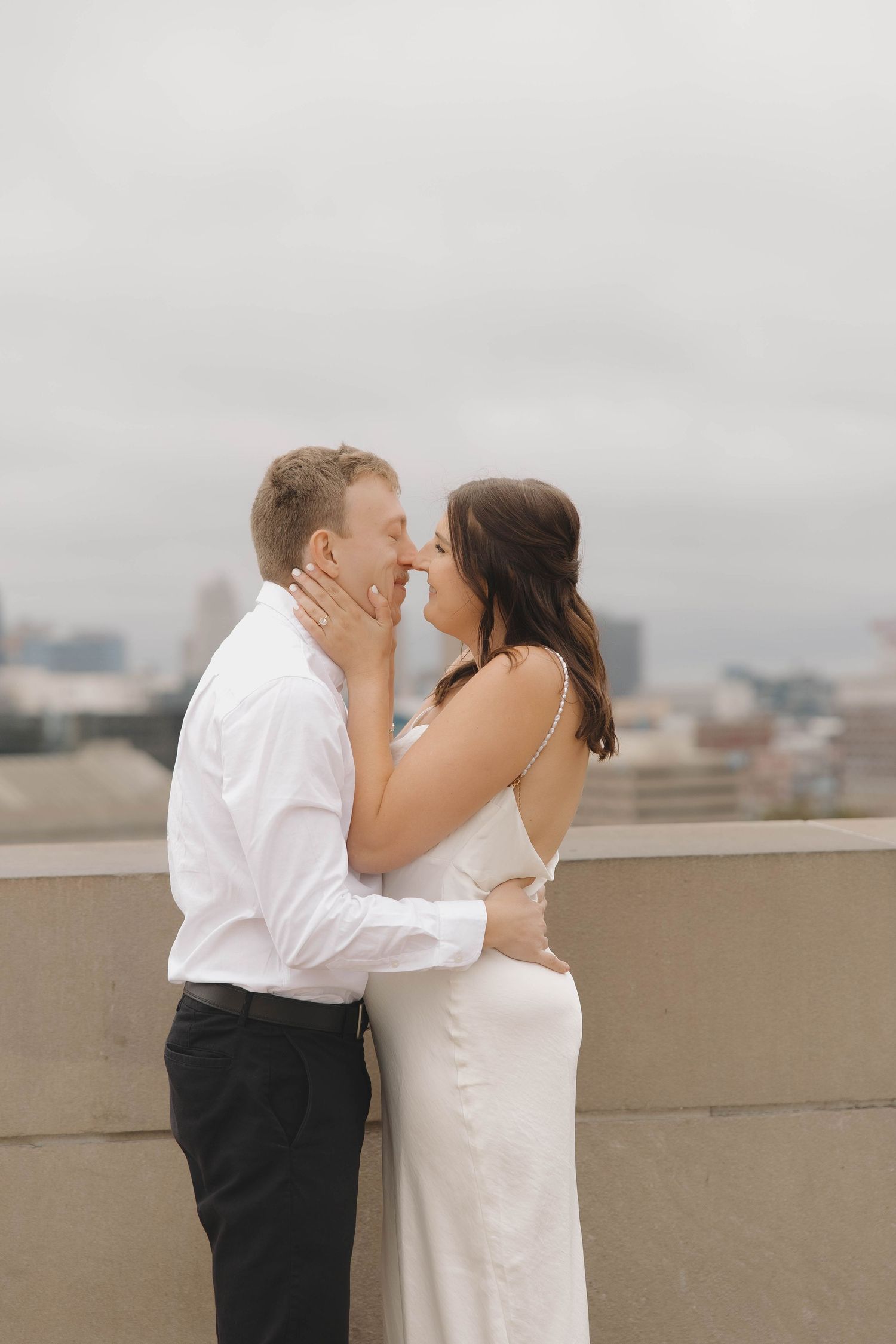 A romantic couple sharing an intimate kiss on a rooftop with a city skyline in the background.