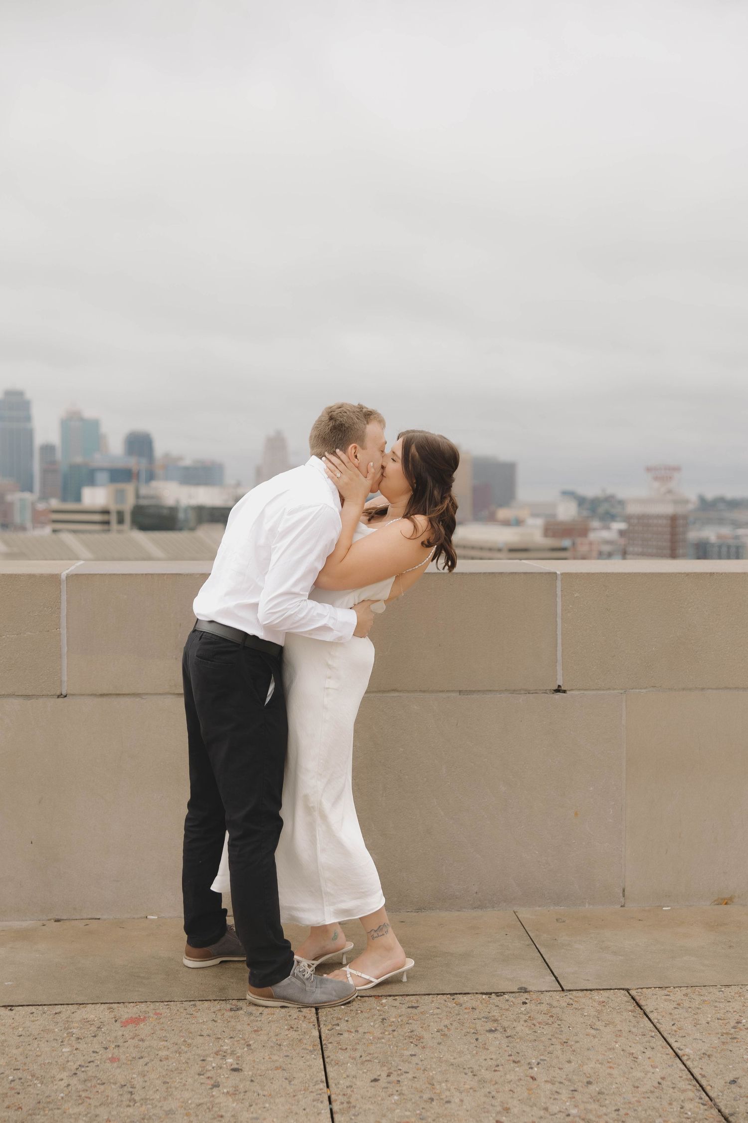 A romantic couple shares a tender kiss on a rooftop overlooking a misty city skyline.
