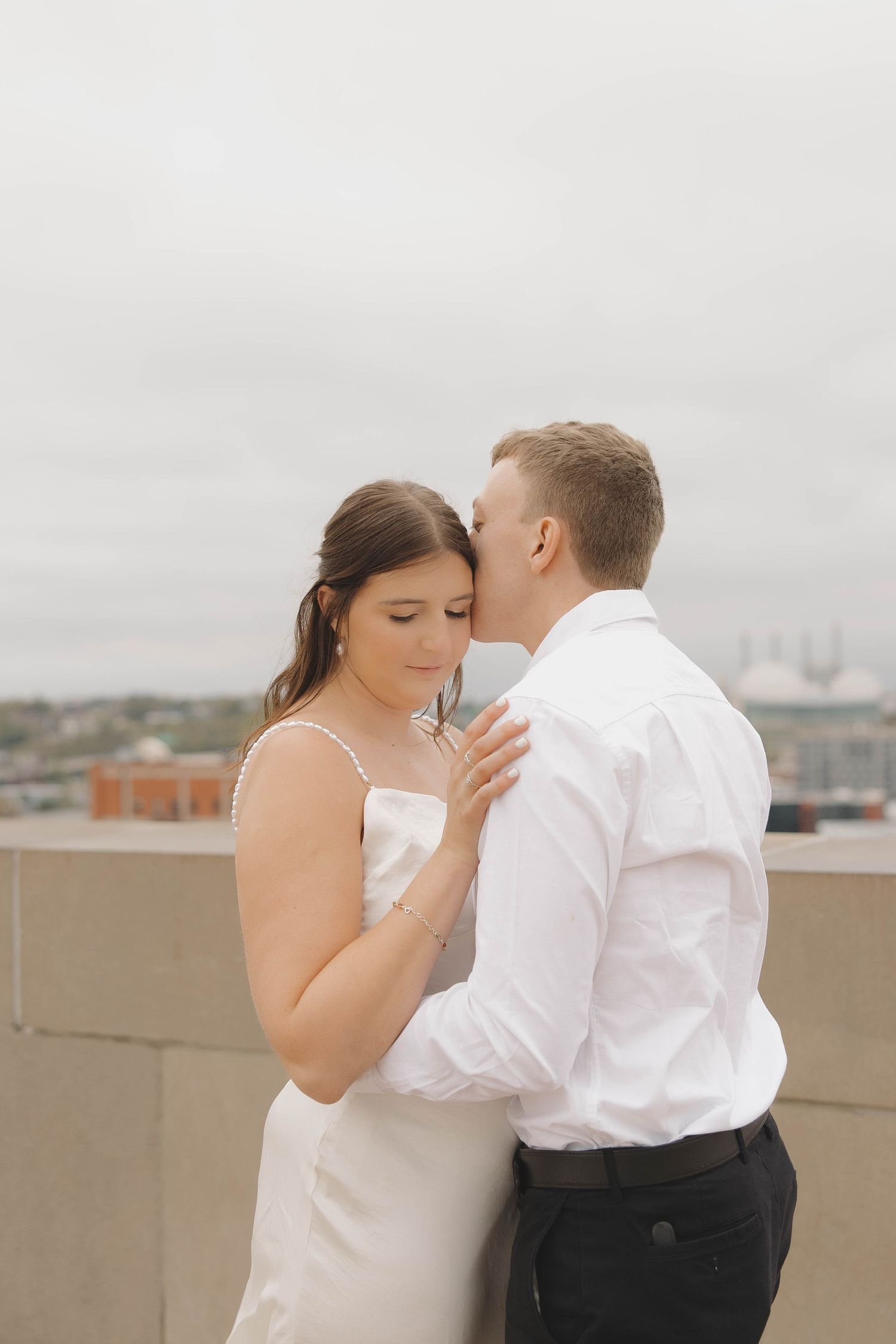 A romantic couple shares an intimate moment on a rooftop with a cityscape in the background.