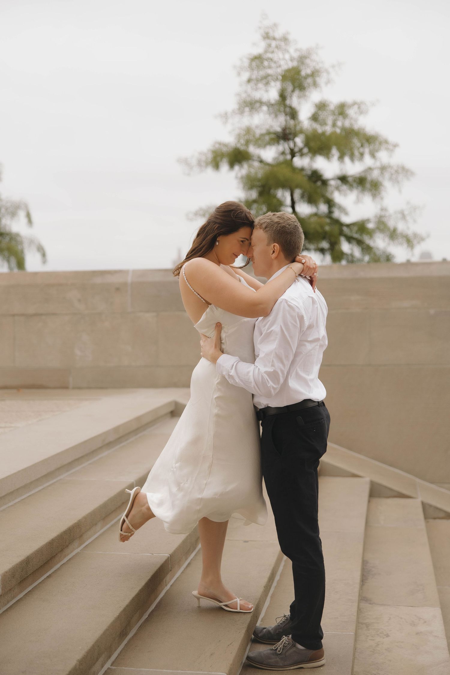 A couple shares a romantic moment on concrete steps during an outdoor photoshoot.