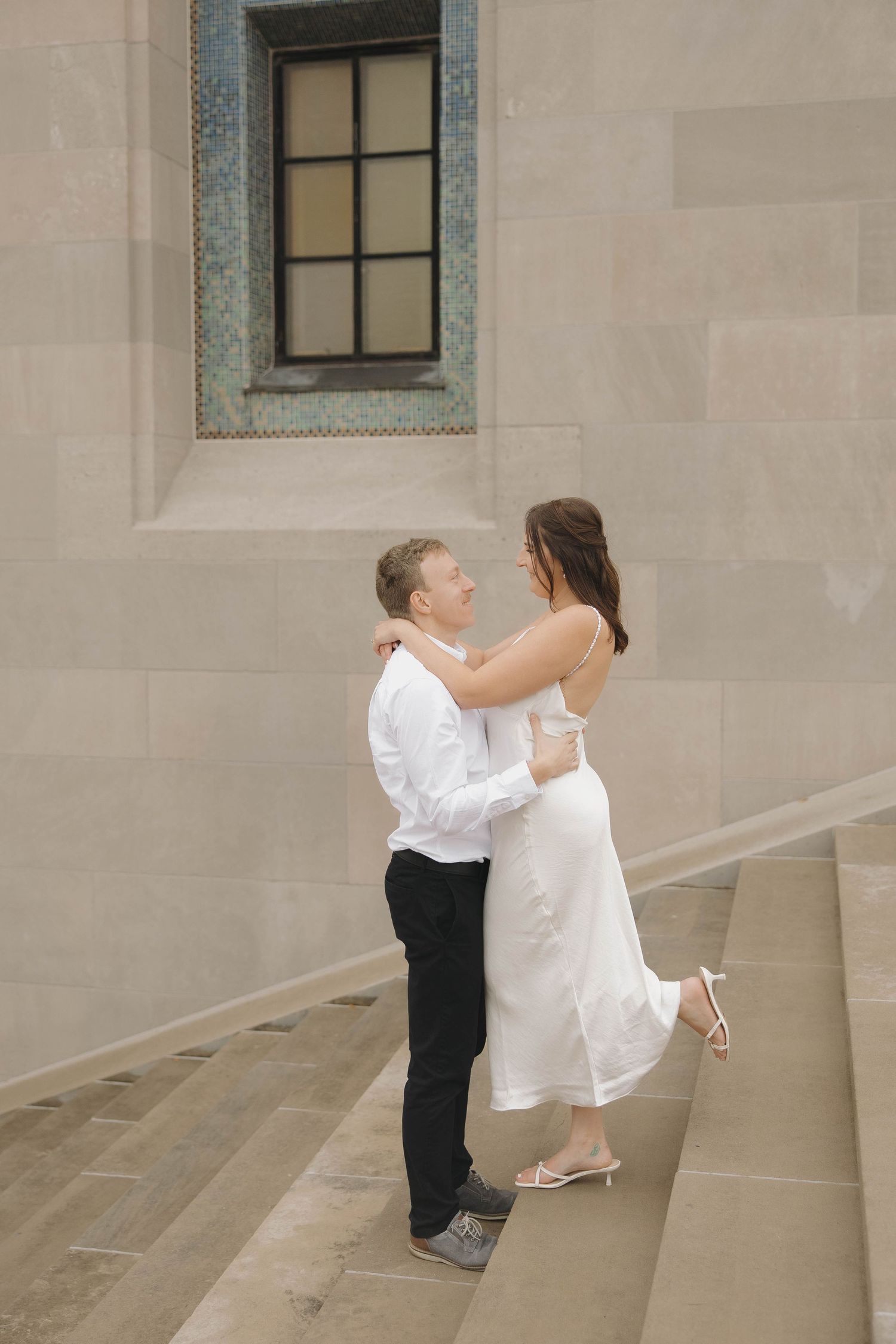 A series of romantic kiss photos between a couple in white attire against a stone building wall.