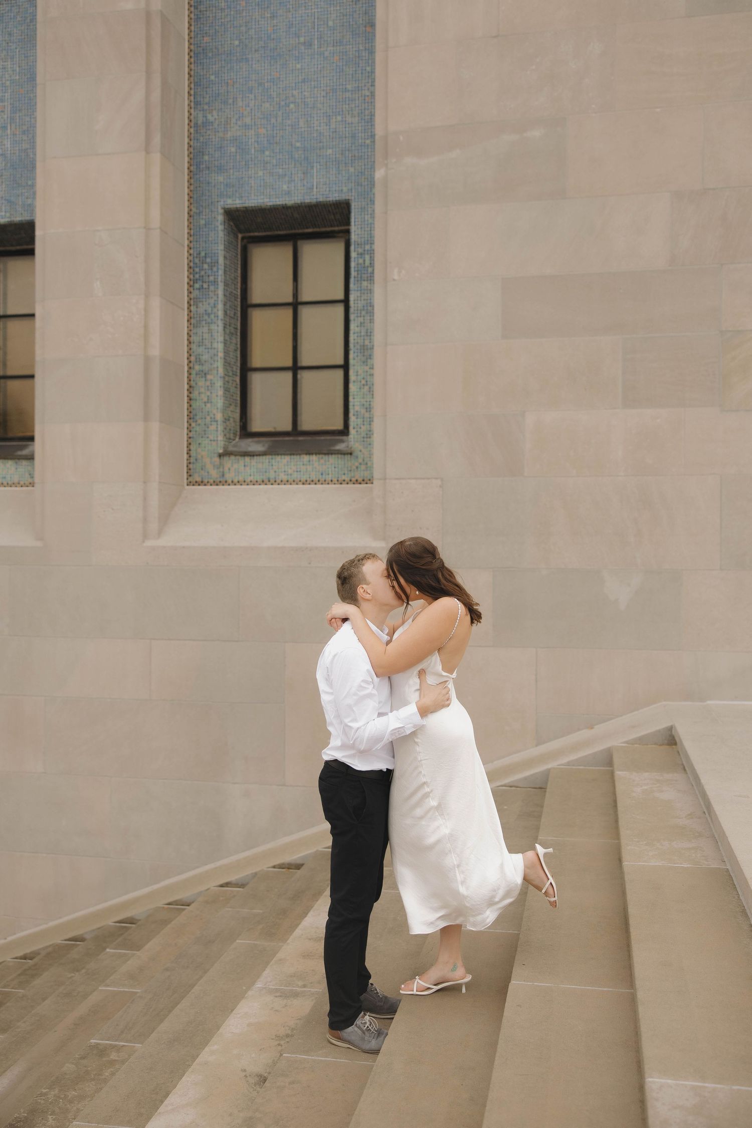 Couple embraces on concrete steps in a romantic moment at an architectural setting.