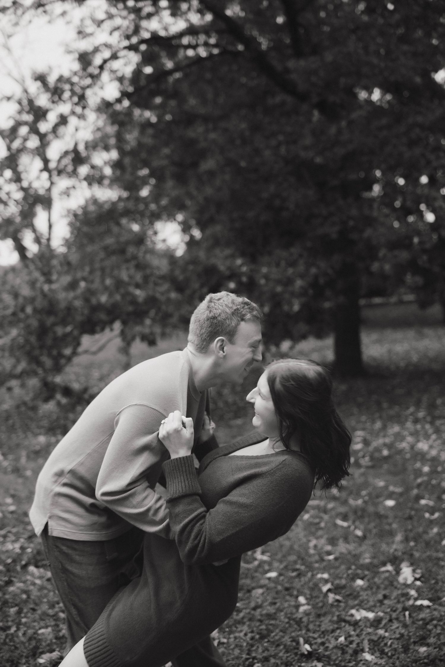 Black and white photo of a playful couple sharing a tender moment in a park.