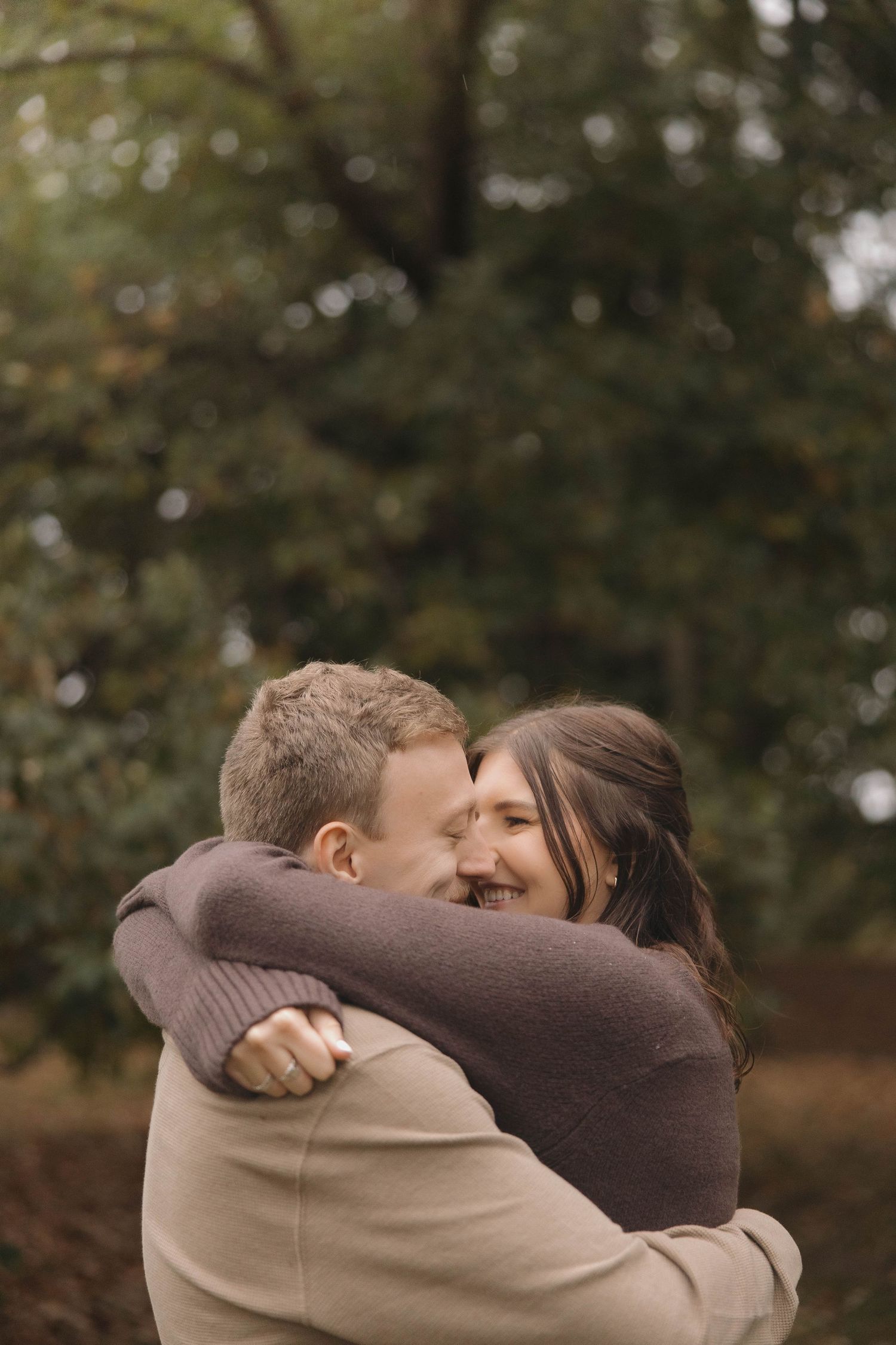 A couple sharing a warm embrace outdoors with autumn trees in the background.