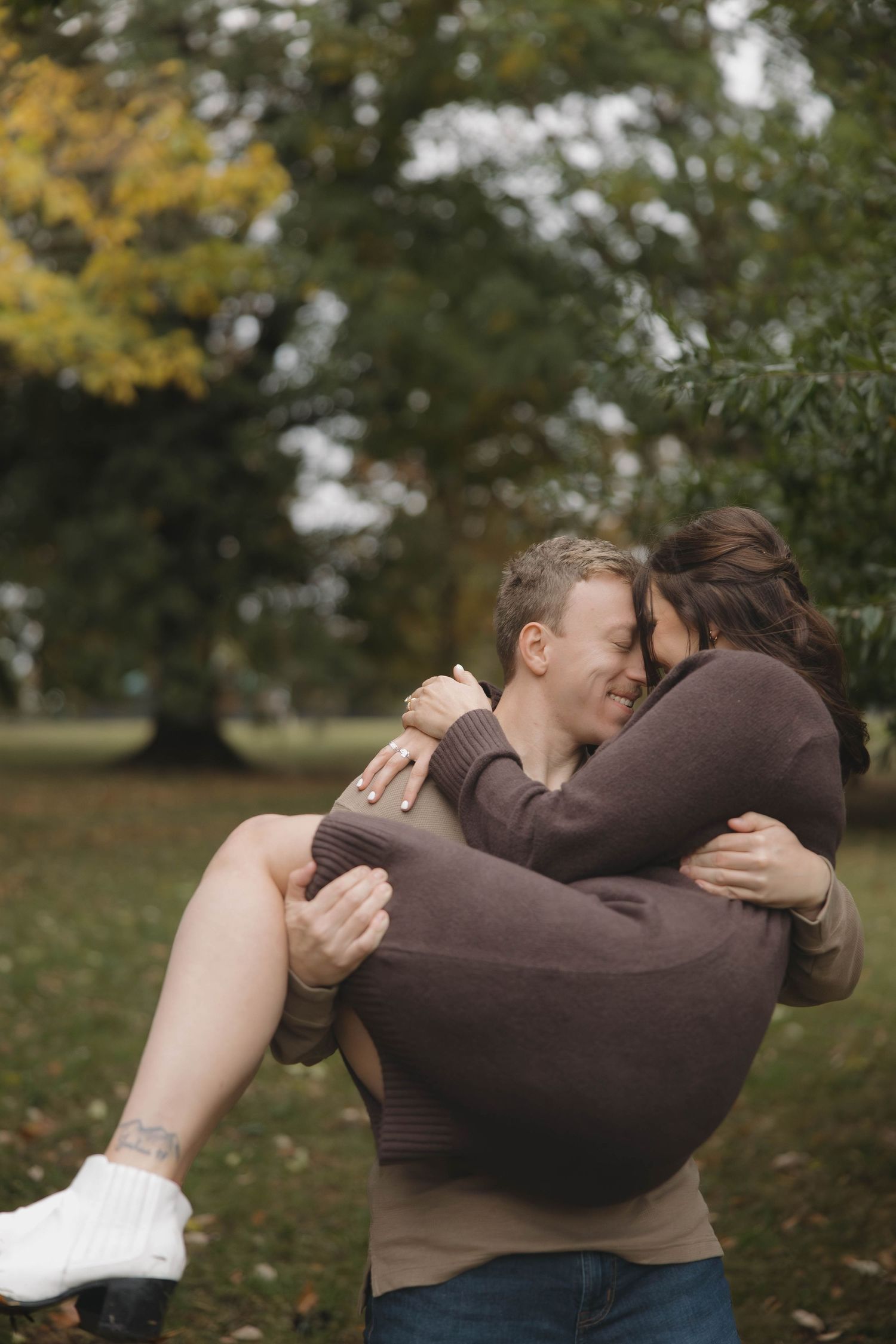 Intimate moment between couple embracing outdoors with fall foliage in background.