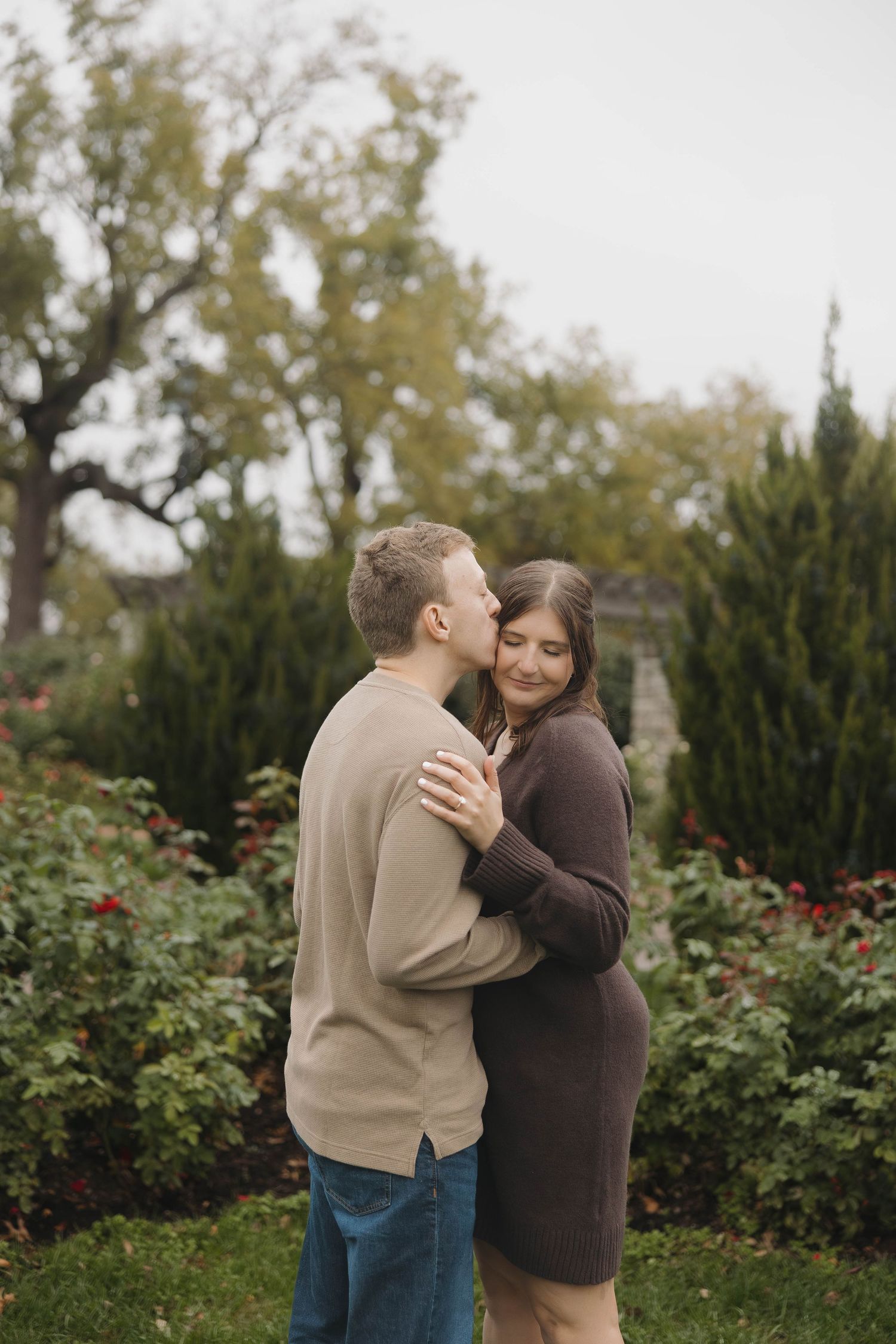 A couple shares a tender moment together in a garden with autumn foliage and rosebushes.