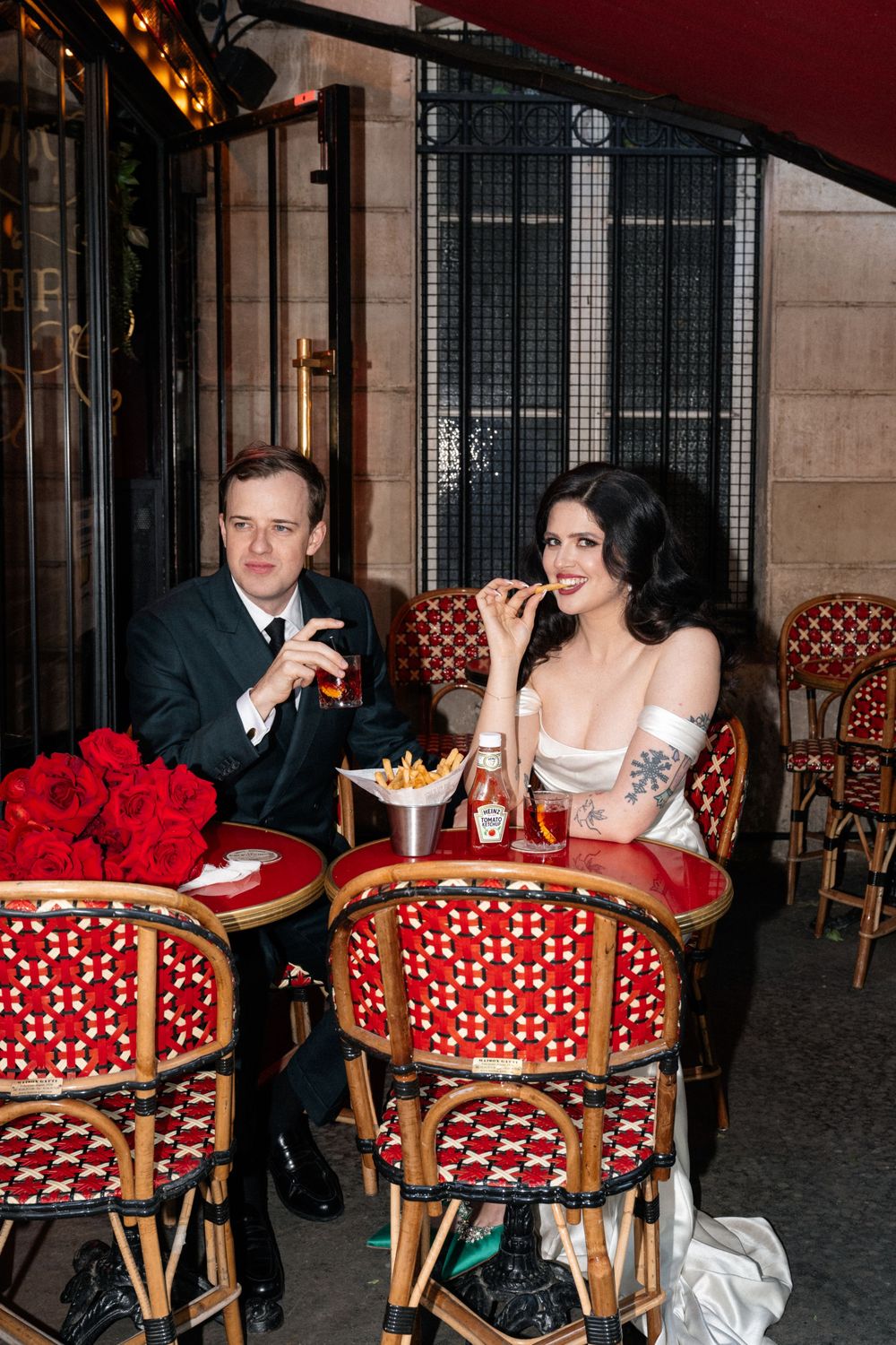 A couple dining at a French bistro with red and white decor, sitting in classic rattan chairs with patterned upholstery.