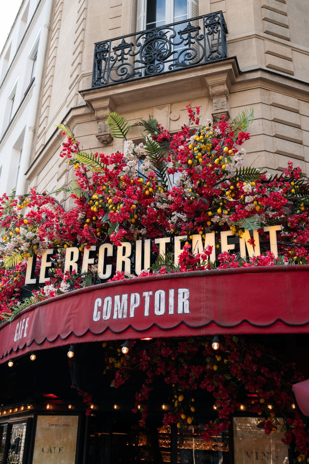Classic French bistro storefront with red awning and vibrant floral arrangements along the facade.