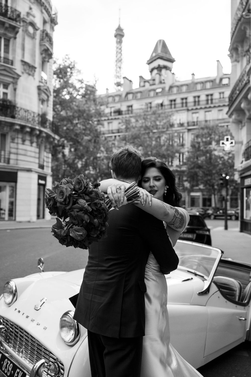 Black and white photo series of newlyweds posing with a vintage white car in a European city setting.