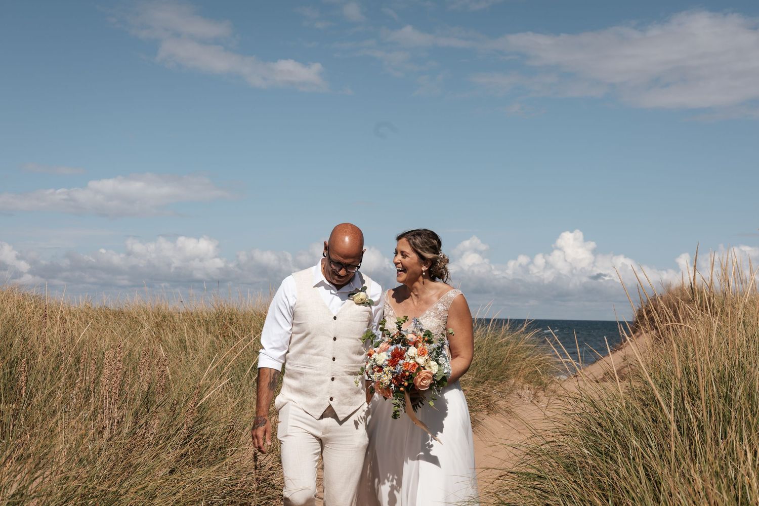 A couple shares romantic moments near a white lighthouse on a sandy beach during sunset.