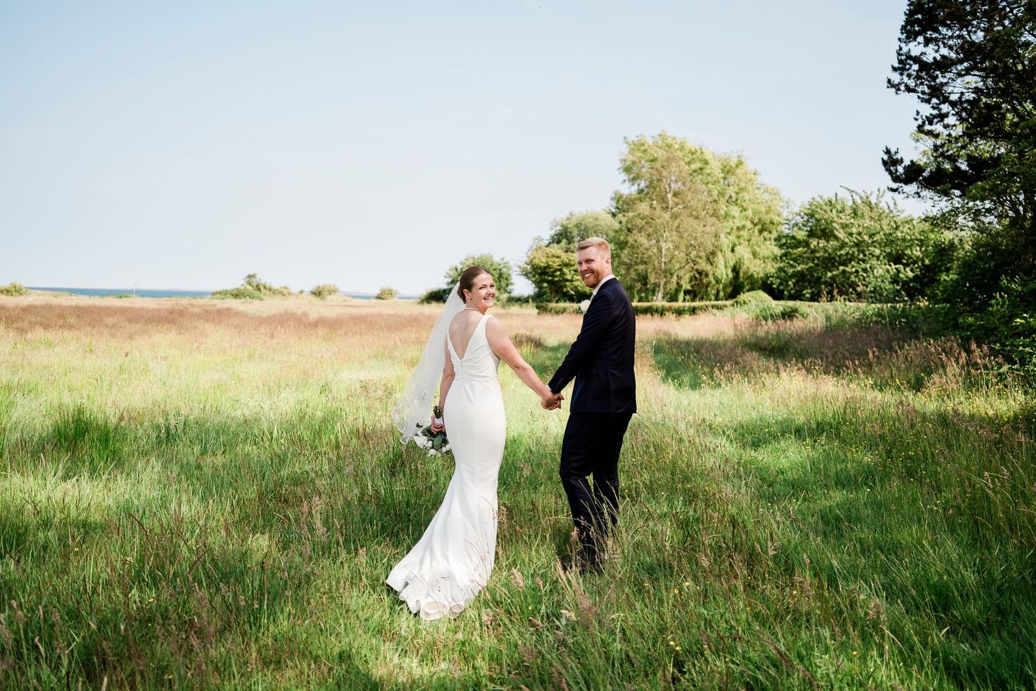 Couple in wedding attire walking through a lush green field on their special day.