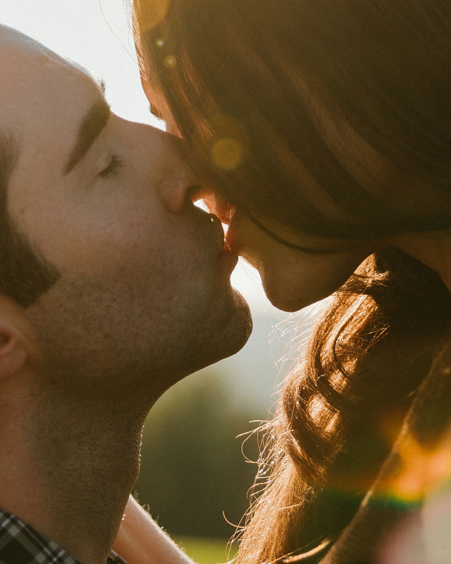 Silhouetted couple sharing an intimate moment at sunset with golden sunlight streaming through their profiles.