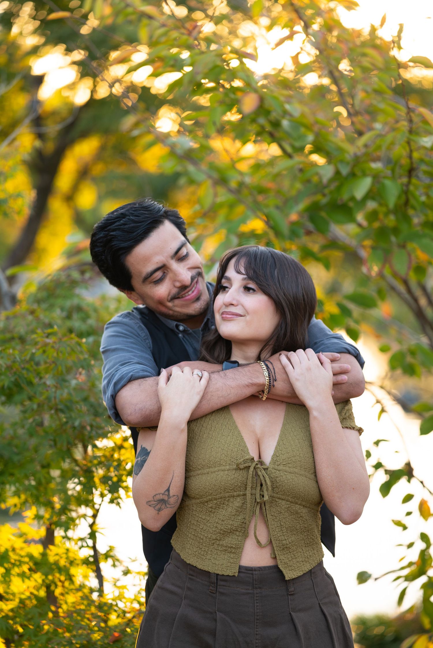 Man lovingly embracing woman from behind amid golden autumn foliage during an engagement photo session.