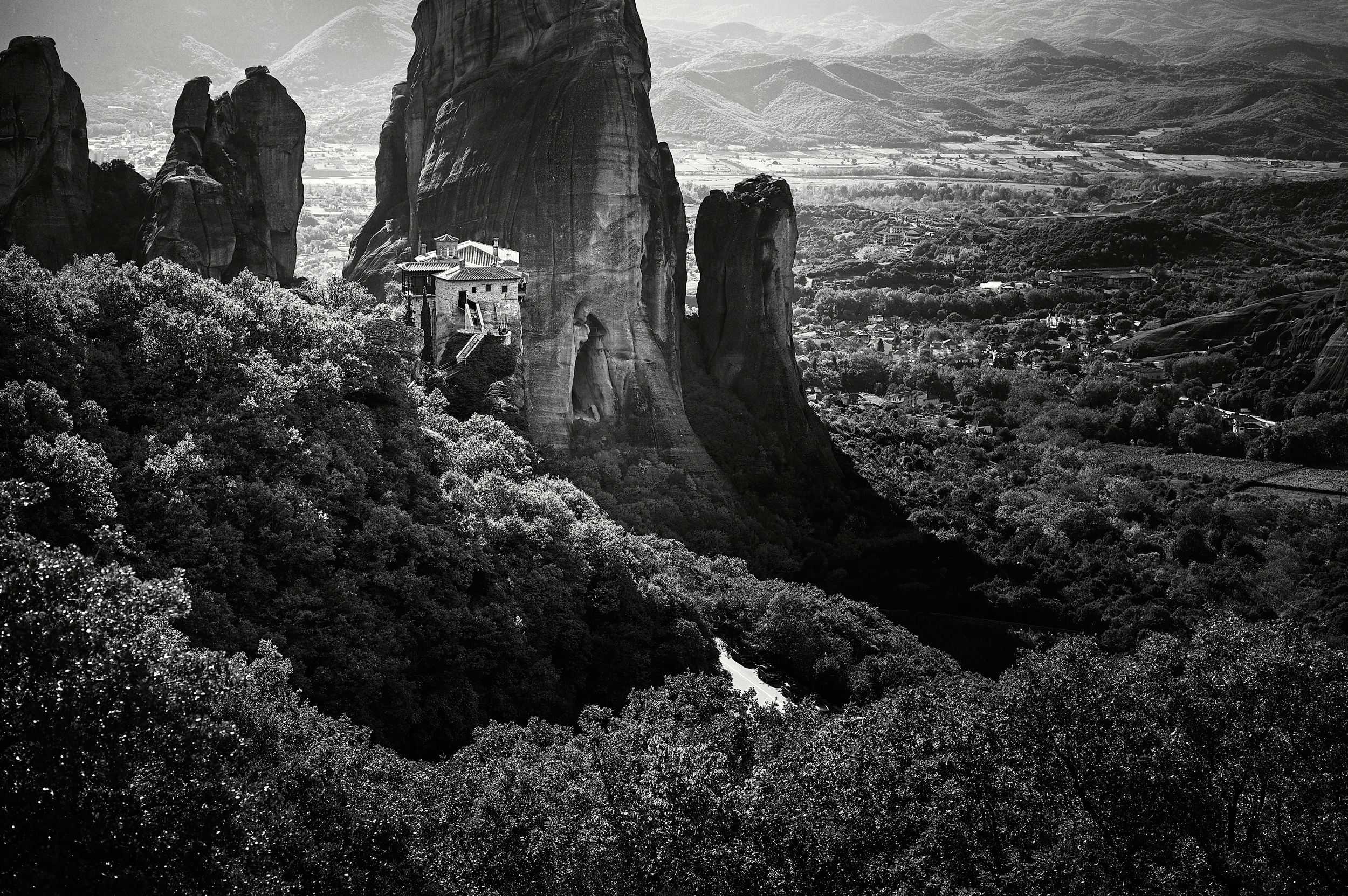A dramatic black and white landscape photo of Meteora's towering rock formations and monasteries in Greece.