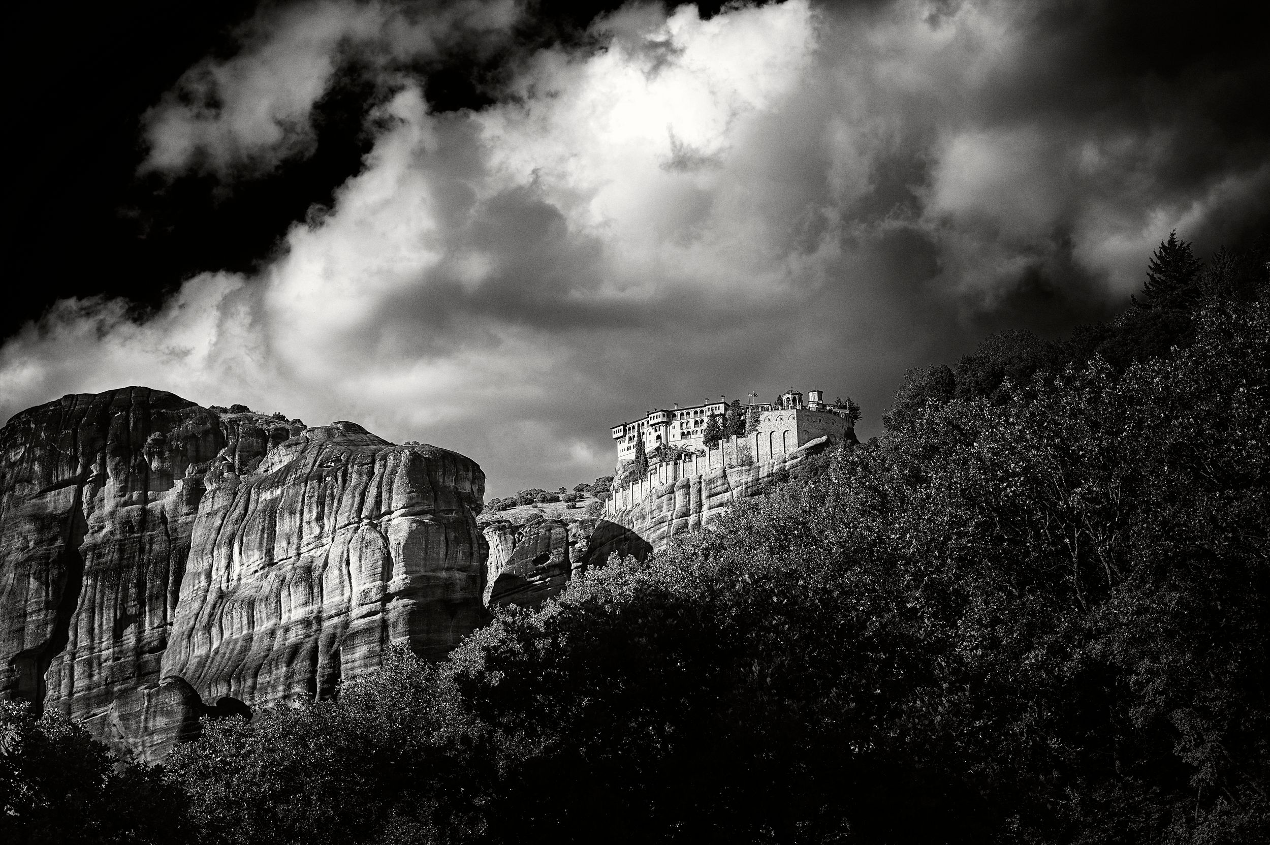 Dramatic black and white panoramic view of Edinburgh Castle perched on a hilltop against moody storm clouds.
