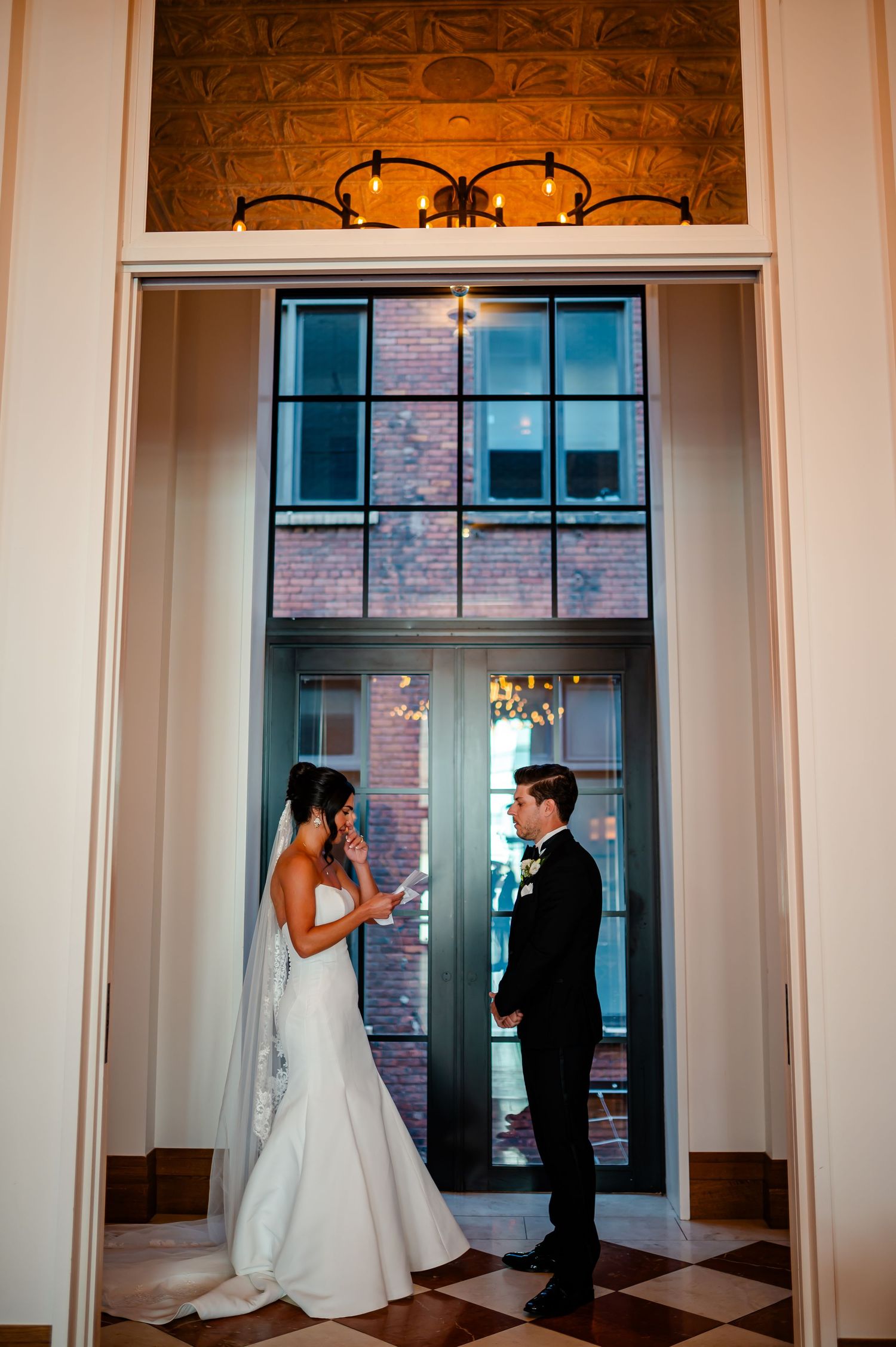 A wedding couple shares their first look in a beautifully lit venue hallway with elegant architectural details.