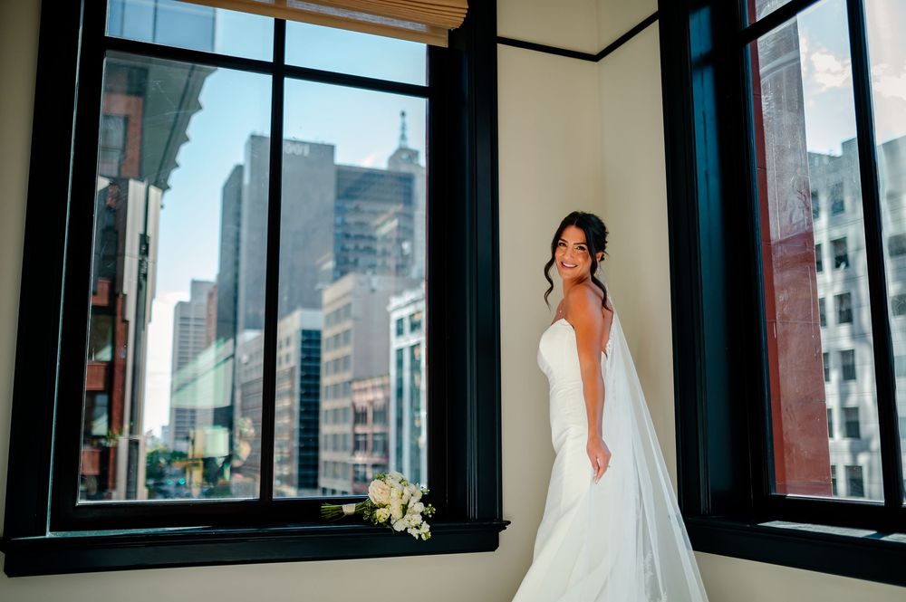 A modern wedding ceremony setup with white chairs and floral arrangements in a bright room with city views through windows.