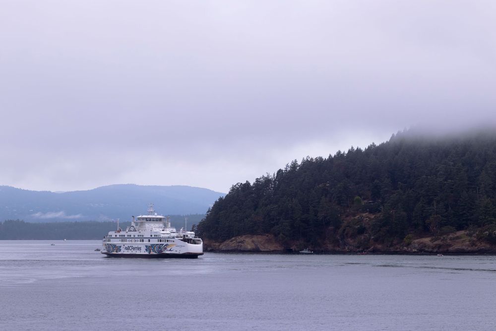 A ferry boat cruises through misty waters near forested islands in the Pacific Northwest.