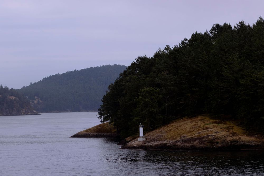 Scenic panoramic view of evergreen forests and islands dotting a tranquil lake with a small lighthouse on the shore.
