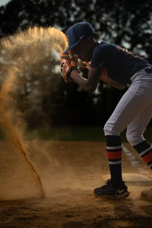 Baseball player slides into base kicking up dramatic clouds of orange dirt and dust at sunset.