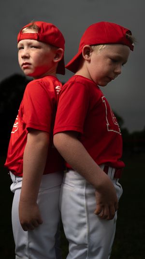 Two young baseball players in red jerseys and gray pants stand back to back in a series of photos.