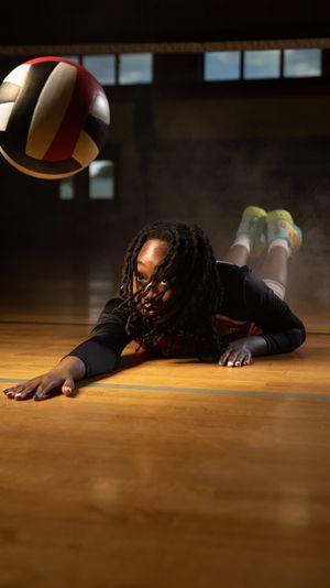 A volleyball player dives across a wooden gym floor to save a ball during an intense match.