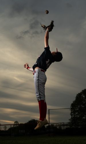 Baseball player silhouetted against dramatic cloudy sky catches ball in outfield during sunset practice session.