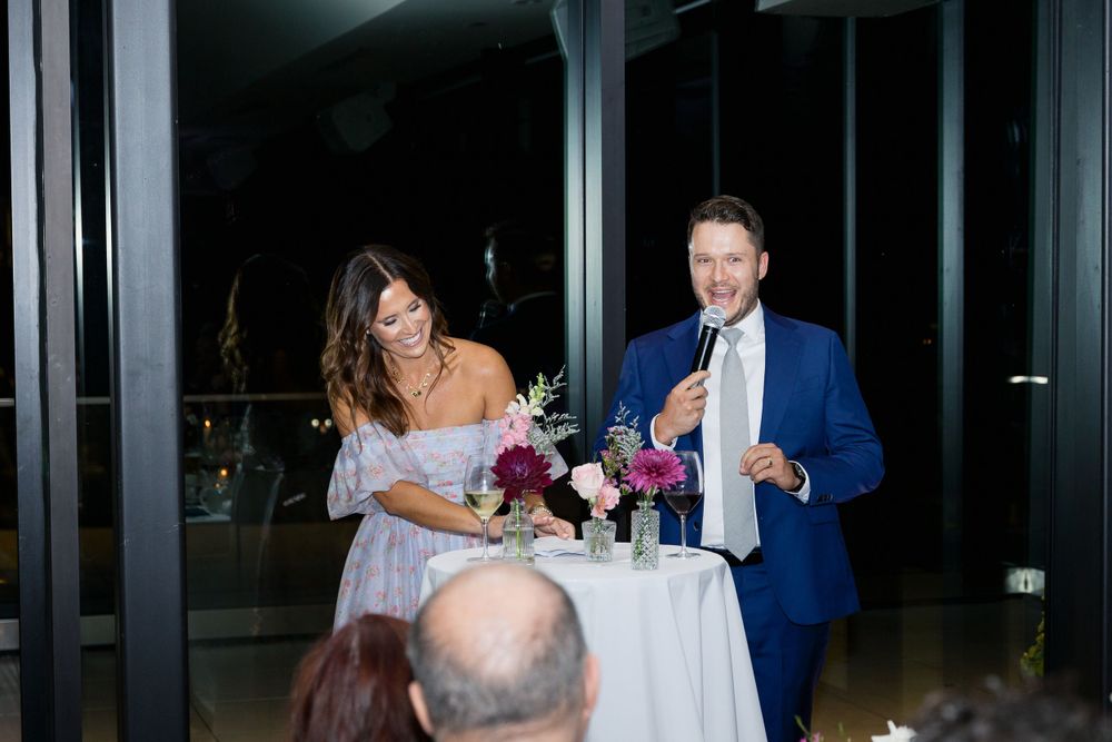 A couple stands next to an elegantly decorated table with floral centerpieces during an evening reception.