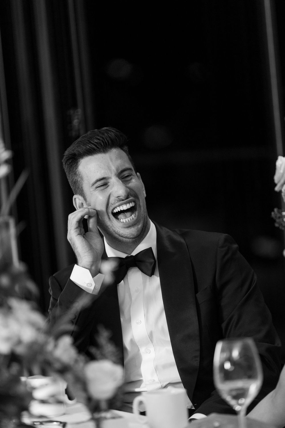 A joyful moment captured in black and white at an elegant dinner party with formal attire and wine glasses on the table.