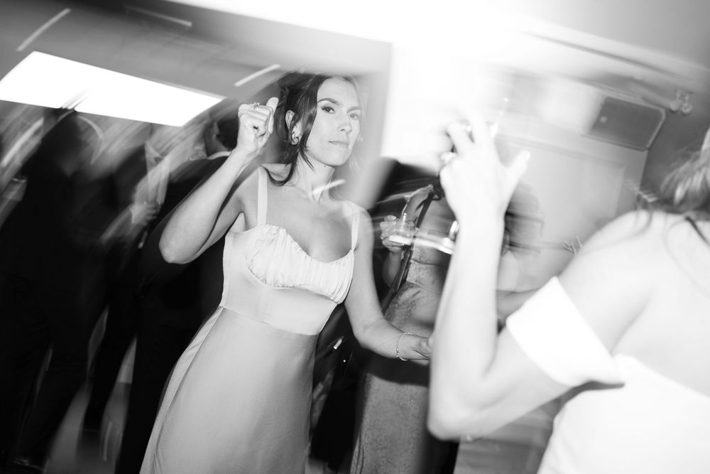 Black and white photograph of people dancing and celebrating at a party with motion blur effects creating a dynamic atmosphere.